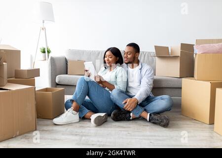 Loving african american spouses using tablet, searching new furniture while sitting among cardboard boxes, free space Stock Photo