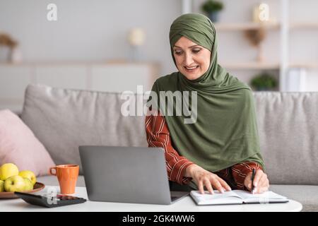 Senior Islamic Businesswoman Taking Notes At Laptop Working At Home Stock Photo