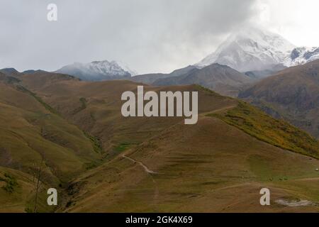 Landscape views of the surrounding mountains in autumn colours and the snow covered peaks in the background from the Sameba Church in Kazbegi, Georgia Stock Photo