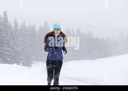 Young slim woman running on the road in the winter snowy morning. Close up portrait of jogging fitness woman with copy space. Stock Photo