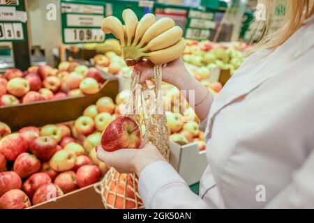 Female hands in a supermarket. Woman put fruits in cotton reusable shopping bag. Close-up. Stock Photo