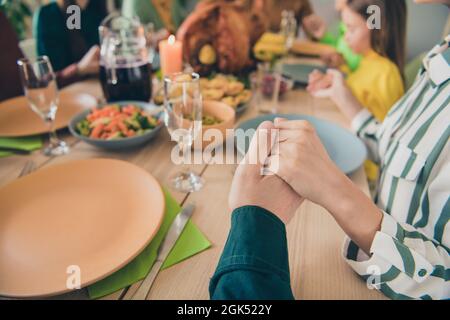 Cropped view portrait of adorable dreamy family holding hands praying appreciating eating lunch at home indoors Stock Photo