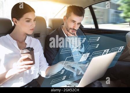 Pensive concentrated successful caucasian millennial business man and woman look at digital hologram on laptop in car Stock Photo