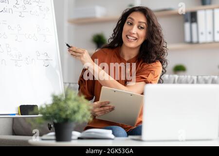 Female teacher explaining math to students using laptop holding clipboard Stock Photo