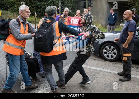 Godstone, UK. 13th September, 2021. A man tries to pull away a banner from Insulate Britain climate activists blocking a slip road from the M25, causing a long tailback on the motorway, as part of a new campaign intended to push the UK government to make significant legislative change to start lowering emissions. The activists, who wrote to Prime Minister Boris Johnson on 13th August, are demanding that the government immediately promises both to fully fund and ensure the insulation of all social housing in Britain by 2025 and to produce within four months a legally binding national plan to fu Stock Photo