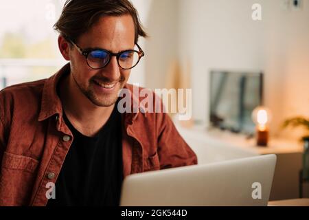Caucasian male student working from home on laptop smiling while finishing project  Stock Photo