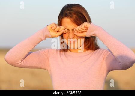 Woman scratching her ithy eyes due allergy in a harvested field Stock Photo