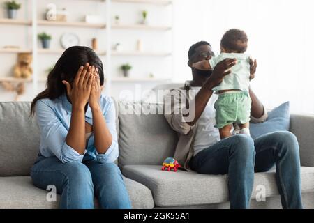 Tired African American mom crying, dad playing with kid Stock Photo