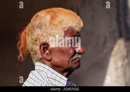 Orchha, Madhya Pradesh, India - March 2019: Candid side profile portrait of an elderly Indian man with orange dyed hair. Stock Photo