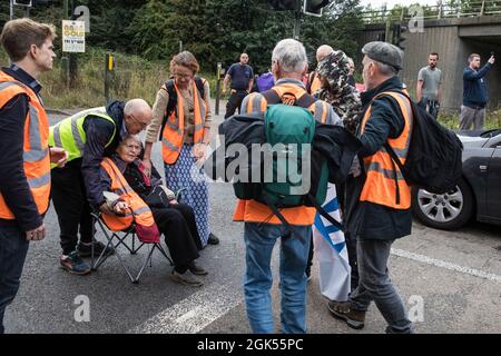 Godstone, UK. 13th September, 2021. A man tries to remove one of several Insulate Britain climate activists blocking a slip road from the M25, causing a long tailback on the motorway, as part of a new campaign intended to push the UK government to make significant legislative change to start lowering emissions. The activists, who wrote to Prime Minister Boris Johnson on 13th August, are demanding that the government immediately promises both to fully fund and ensure the insulation of all social housing in Britain by 2025 and to produce within four months a legally binding national plan to full Stock Photo