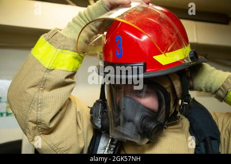 Hull Maintenance Technician Fireman Zachary Brinks, from Salcha, Alaska, assigned to USS Gerald R. Ford's (CVN 78) engineering department, dons a firefighting ensemble during a general quarters drill, August 5, 2021. Ford is underway in the Atlantic Ocean conducting Full Ship Shock Trials. The U.S. Navy conducts shock trials of new ship designs using live explosives to confirm that our warships can continue to meet demanding mission requirements under the harsh conditions they might encounter in battle. Stock Photo