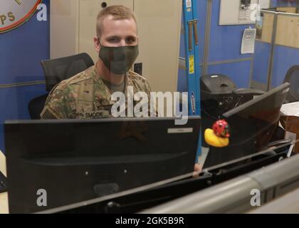 Army Reserve Spc. Noah Smok, an information technology specialist, or 25 Bravo, mans the computer and telecommunications Help Desk at 1st Theater Sustainment Command's operational command post, wearing his face mask and behind a plastic shield--all part of the 1st TSC-OCP's COVID-19 mitigation protocols. Smock deployed to the 1st TSC-OCP at Camp Arifjan, Kuwait, with other "Brickyard" Soldiers of the Indianapolis-based 310th Sustainment Command (Expeditionary), who staff the 1st TSC-OCP during their nine-month rotation that began December 2020. Stock Photo