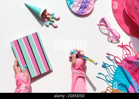 Collection of party objects and sweets on geometric paper flat lay. Chocolate, candy. Notebook and rainbow pen in hand. Geometric layered background Stock Photo