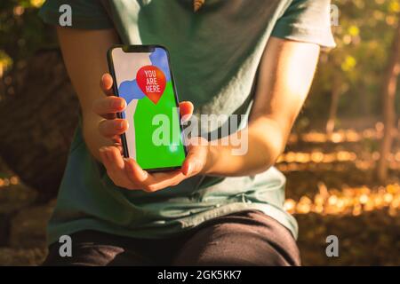 Woman using mobile phone for navigation in forest. Screen with maps and you are here sign Stock Photo