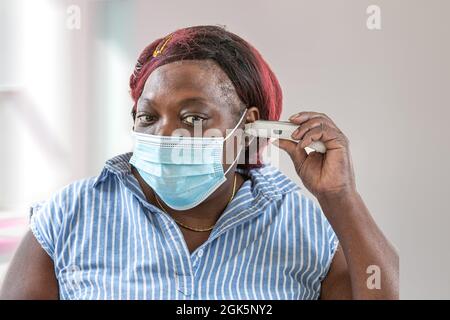 Fever and coronavirus symptoms, woman in medical mask measures body temperature. Stock Photo