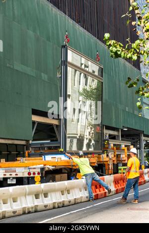 Construction workers guiding a giant glass window pane for installation in a skyscraper on Fifth Avenue, New York City, USA  2021 Stock Photo