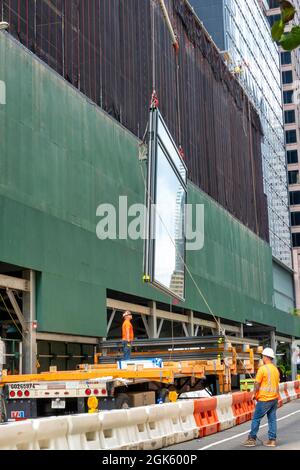 Construction workers guiding a giant glass window pane for installation in a skyscraper on Fifth Avenue, New York City, USA  2021 Stock Photo