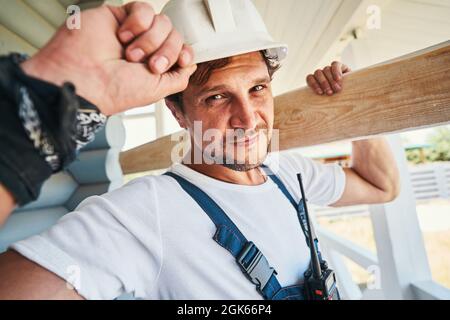 Hard-working builder adjusting his hard hat while carrying board Stock Photo