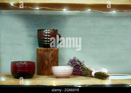 Still life in Provence style. Clay cup on a wooden stand and a bunch of lavender on the background of a green wall. Stock Photo