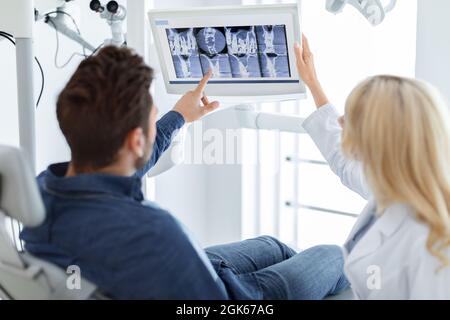 Dentist having conversation with male patient, looking at LED display Stock Photo