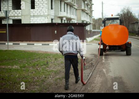 A worker washes the road from a hose. Cleaning of the territory. Washing off dirt from asphalt. Municipal service in the city. Stock Photo