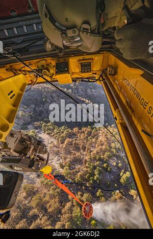 U.S. Army crew chief Pvt. Austin Custer, assigned to Bravo Company, 1st Battalion, 214th Aviation Regiment, 12th Combat Aviation Brigade, releases water from a bucket attached to a CH-47 Chinook as the crew flies Western Turkey during an aerial firefighting mission Aug. 14, 2021. The pilots direct the Custer when it’s time to release the water. Stock Photo