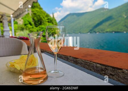 rose wine flute by the lakefront of Lugano city in Switzerland. Romantic appetizer in Ticino Canton on Swiss Lake Lugano of Switzerland. Olive trees Stock Photo