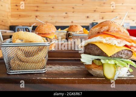 Frontal view of various types of hamburgers and their accompaniments in metal baskets, placed on wooden tables and with a pine wood background Stock Photo