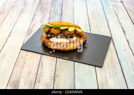 Venezuelan shredded chicken arepa with fresh cheese, ripe banana, avocado slices and black beans on black slate tray Stock Photo