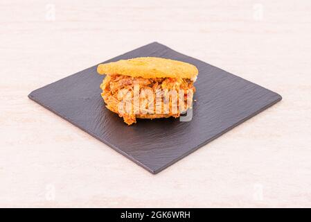Classic Venezuelan arepa with shredded meat on black slate square plate Stock Photo