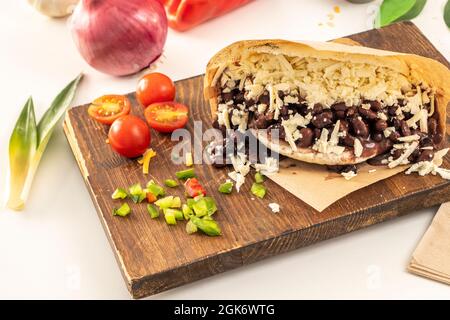 Venezuelan domino arepa with black beans and lots of grated cheese on wooden board and fresh kitchen seasonings on white background Stock Photo