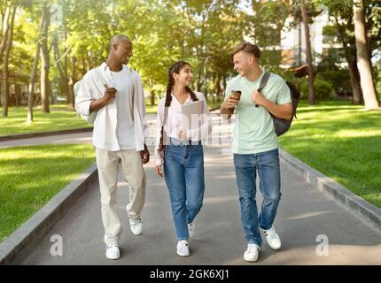 Three multiracial high-school students walking after study and talking in university campus outdoors Stock Photo