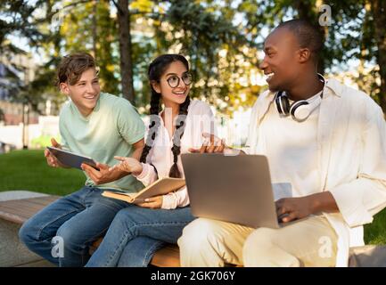 Students lifestyle. Three university friends learning together, using laptops and reading book, sitting in campus Stock Photo