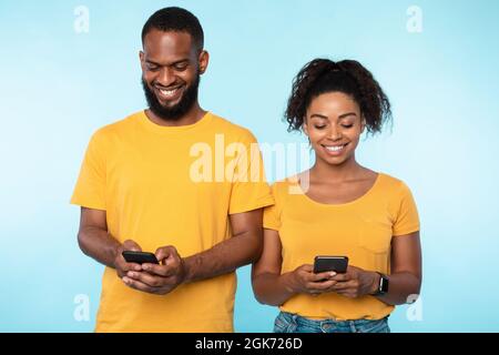 Young black couple using cellphones, surfing web, posting in social media, checking email messages on blue background Stock Photo