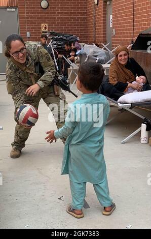 KABUL, AFGHANISTAN - Specialist Julie Bailey with XVIII Airborne Corps' 82nd Airborne Division plays catch with an Afghan child at Hamid Karzai International Airport.    Soldiers supporting the noncombatant evacuation operation demonstrate the kind of empathy and humanity that anyone would desire in this dark moment. Stock Photo