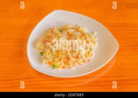 Three delicious rice typical of a Chinese restaurant with fried egg filaments, pieces of carrot, ham and peas on an orange table Stock Photo