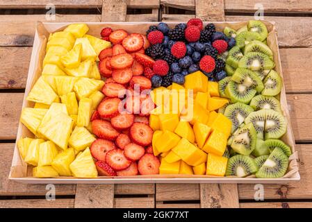 large tray of chopped assorted fruits with pineapple, mango, kiwi, strawberries and red berries in fruit boxes Stock Photo