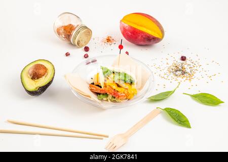 Bao bread with large shrimp inside and props of mango, avocado, chopsticks and wooden forks in container for home delivery Stock Photo