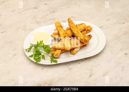 Chopped aubergines like fried fingers in tempura with dip sauce and fresh parsley on a white plate. Stock Photo