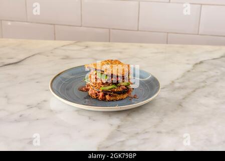 Sandwich of fried aubergine slices presented in layers with chicken pull filling and vegetables on marble table Stock Photo