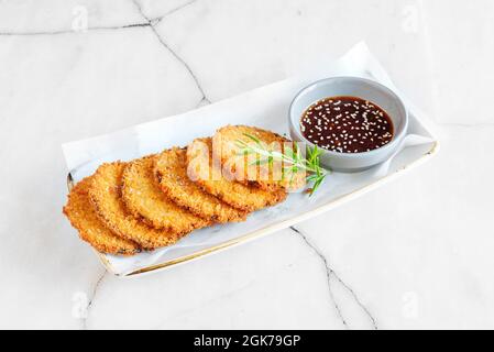 Eggplant battered with egg and breadcrumbs with a sprig of rosemary and soy sauce with sesame seeds to dip Stock Photo