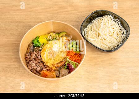 Bibimbap takeaway bowl with udon noodles with fried egg, edamame beans, meat and vegetables Stock Photo