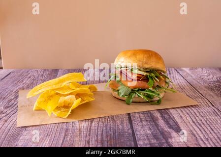 Fish burger with brioche bread with smoked salmon, arugula, ripe avocado, dill salsa and fried banana chips Stock Photo