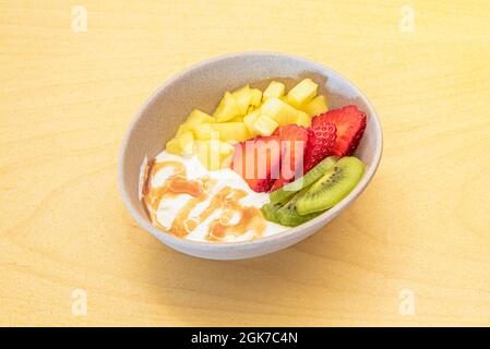 https://l450v.alamy.com/450v/2gk7c4n/bowl-of-fresh-fruits-with-yogurt-and-syrup-pineapple-kiwi-and-chopped-strawberries-on-yellow-table-2gk7c4n.jpg
