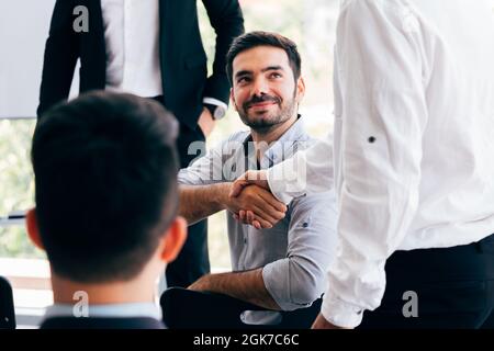 Close-up of two businessmen shaking hands together in indoor office environment - business greeting, success, teamwork concept Stock Photo