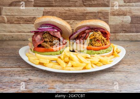 Tasting of shredded chicken and beef burgers with large rings of raw purple onion with a base of guacamole, melted cheese, tomato slices and fried bac Stock Photo