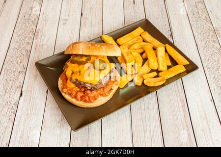 Mexican chili de carne burger with beans and jalapenos with melted cheddar cheese and chips on black plate Stock Photo