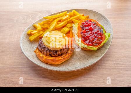 Burgers menu with veal, fried goat cheese, grilled brioche bread and tomato jam with caramelized onion on lettuce and fried garnish potatoes Stock Photo