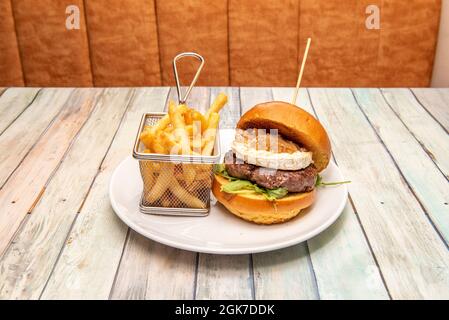 Beef burger with grilled brioche bread, goat cheese, stewed onion, arugula and fried potatoes in a metal basket Stock Photo