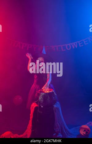 Little witch child cooking potion in the cauldron on Halloween. Stock Photo